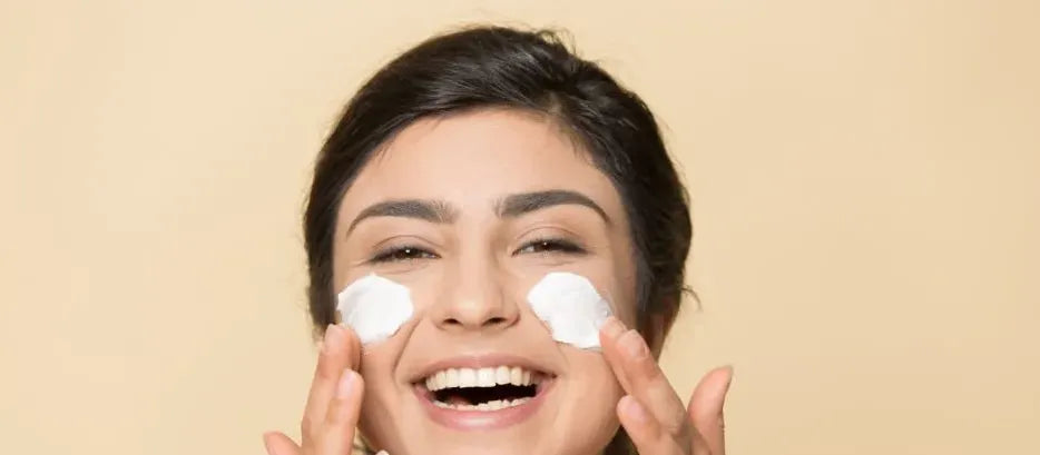 A woman applying moisturizer to her face, showcasing effective skin care tips for combating winter dryness.