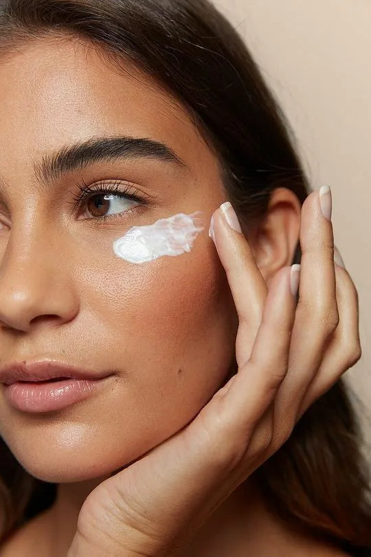 A woman applying oil-free moisturizer to her face, promoting clear and healthy skin.